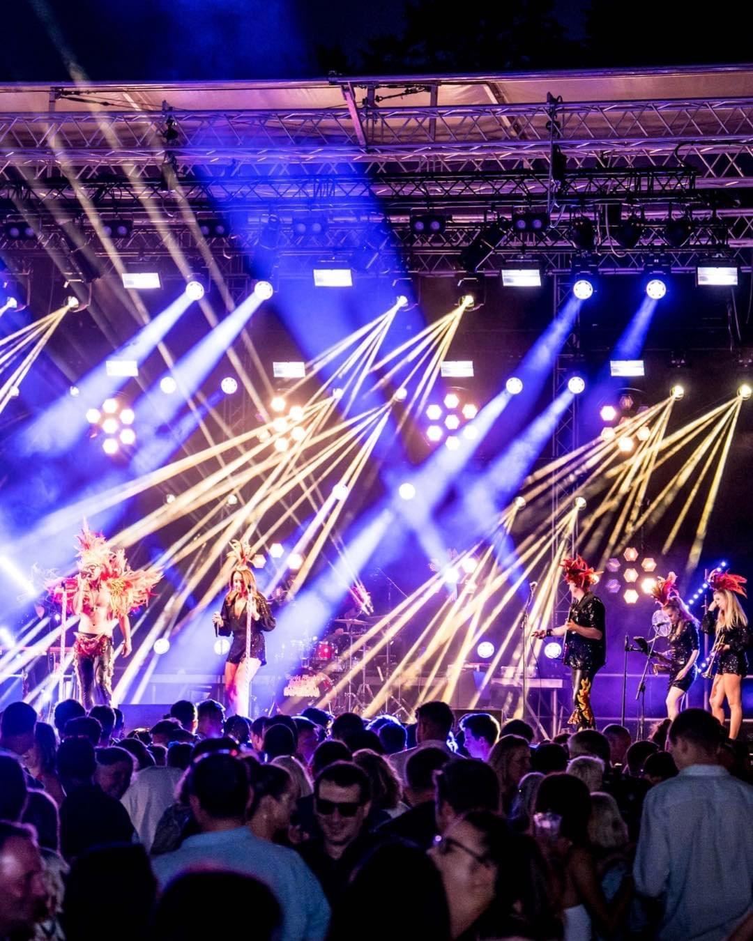 Uncle Funk on a festival stage at night under a fan of blue and gold beams, crowd packed in front