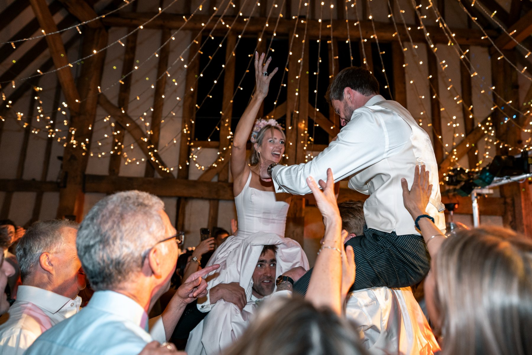 Bride and groom lifted together beneath a canopy of golden fairy lights