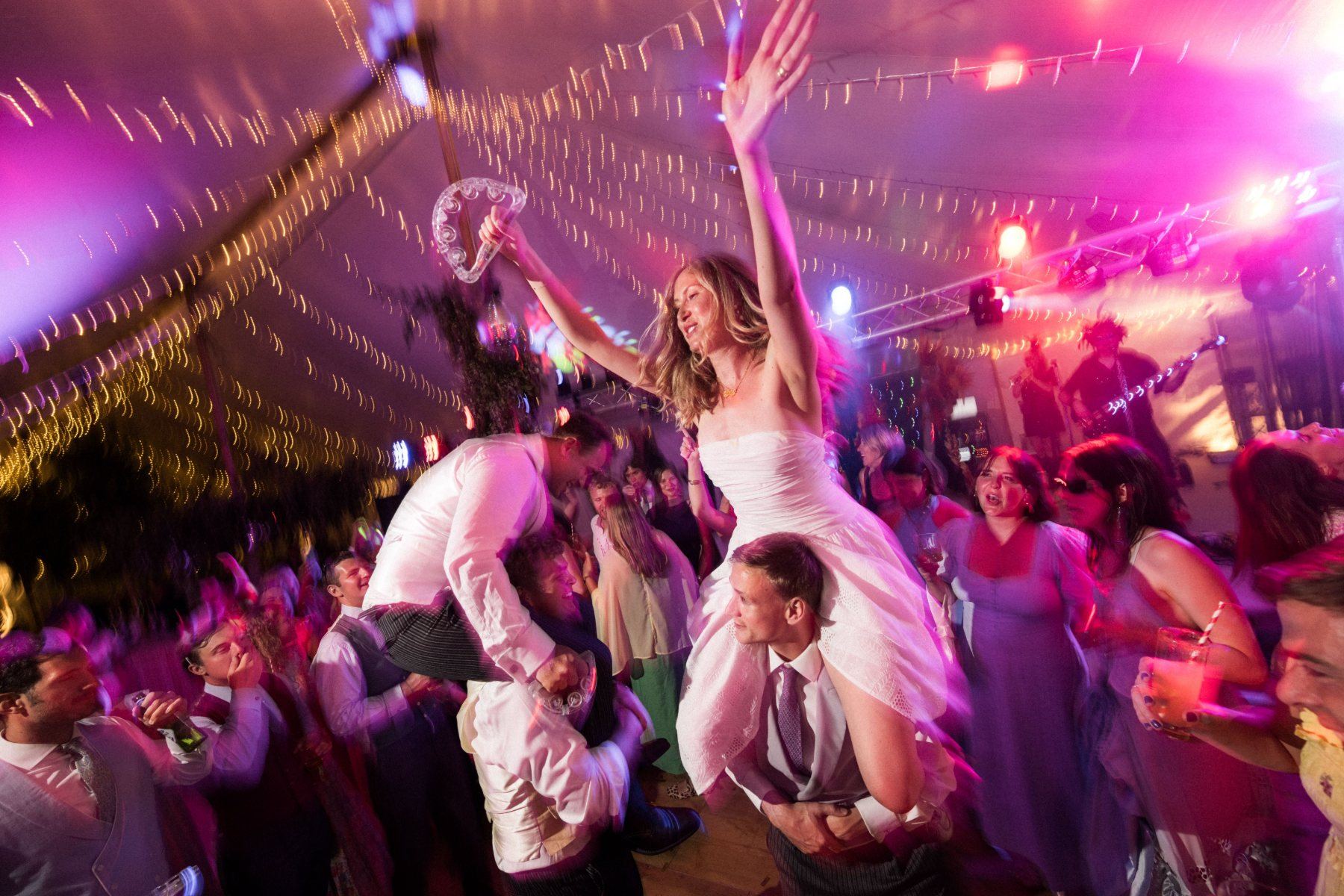 Bride lifted high above the marquee dancefloor, one arm thrown up with a tambourine