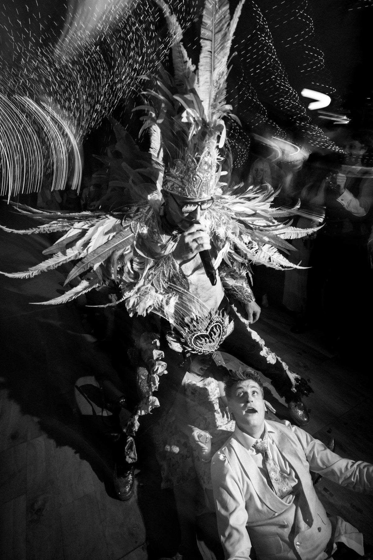 Bride sitting back on the dancefloor mid song, tambourine held high, the frontman singing over her in feathers