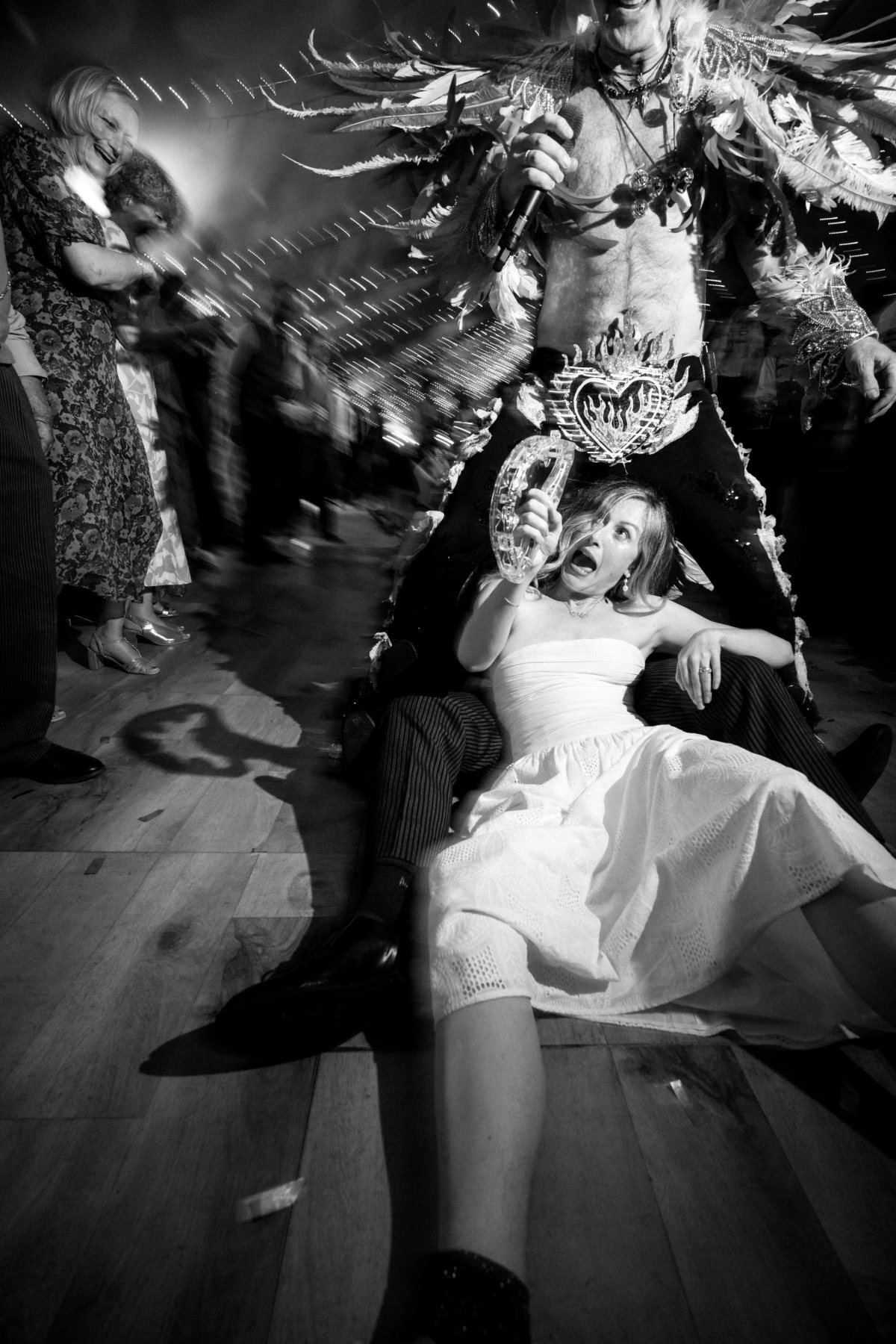 The frontman in a full feathered headdress singing down into a wedding crowd, light trails spinning behind him